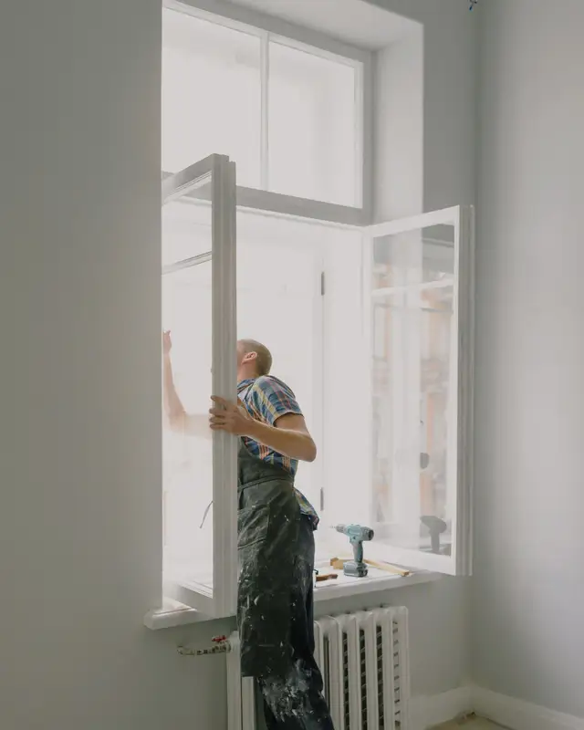 Installer on a step reaching up to fit a tall window frame in a white room