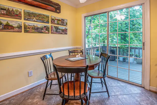 Dining room with a wide sliding glass door opening onto a wooden deck and trees