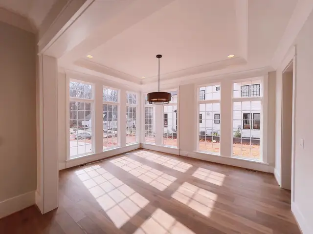 Sunlit room with tall glass doors and windows casting light across a wood floor